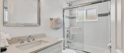 Een moderne badkamer met een douche met glazen wand, een grote spiegel en een witte wastafel.