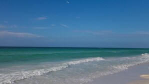 Ein Strand mit klarem türkisblauem Wasser, sanften Wellen und wolkenlosem Himmel.