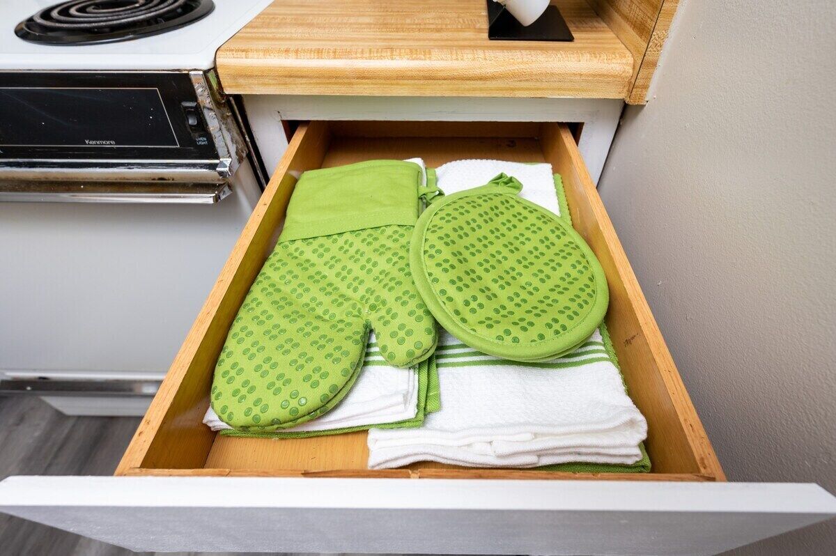 A drawer containing green oven mitts and a white towel.