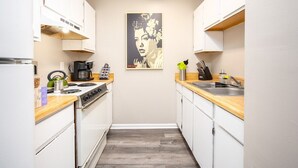 A compact kitchen with white cabinets, a wooden countertop, a stove, a sink, and a poster on the wall.