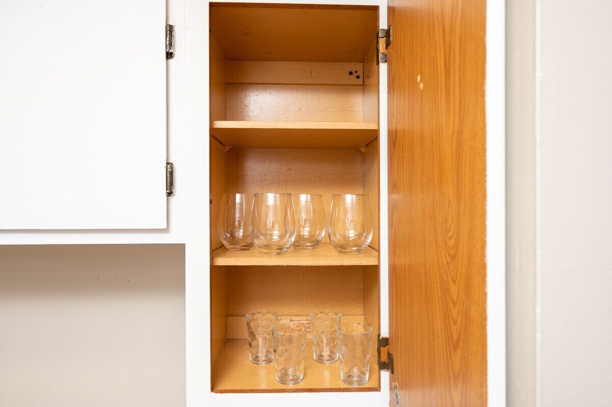 Un mueble de madera con dos estantes, uno con vasos transparentes y el otro con vasos pequeños con diseños.
