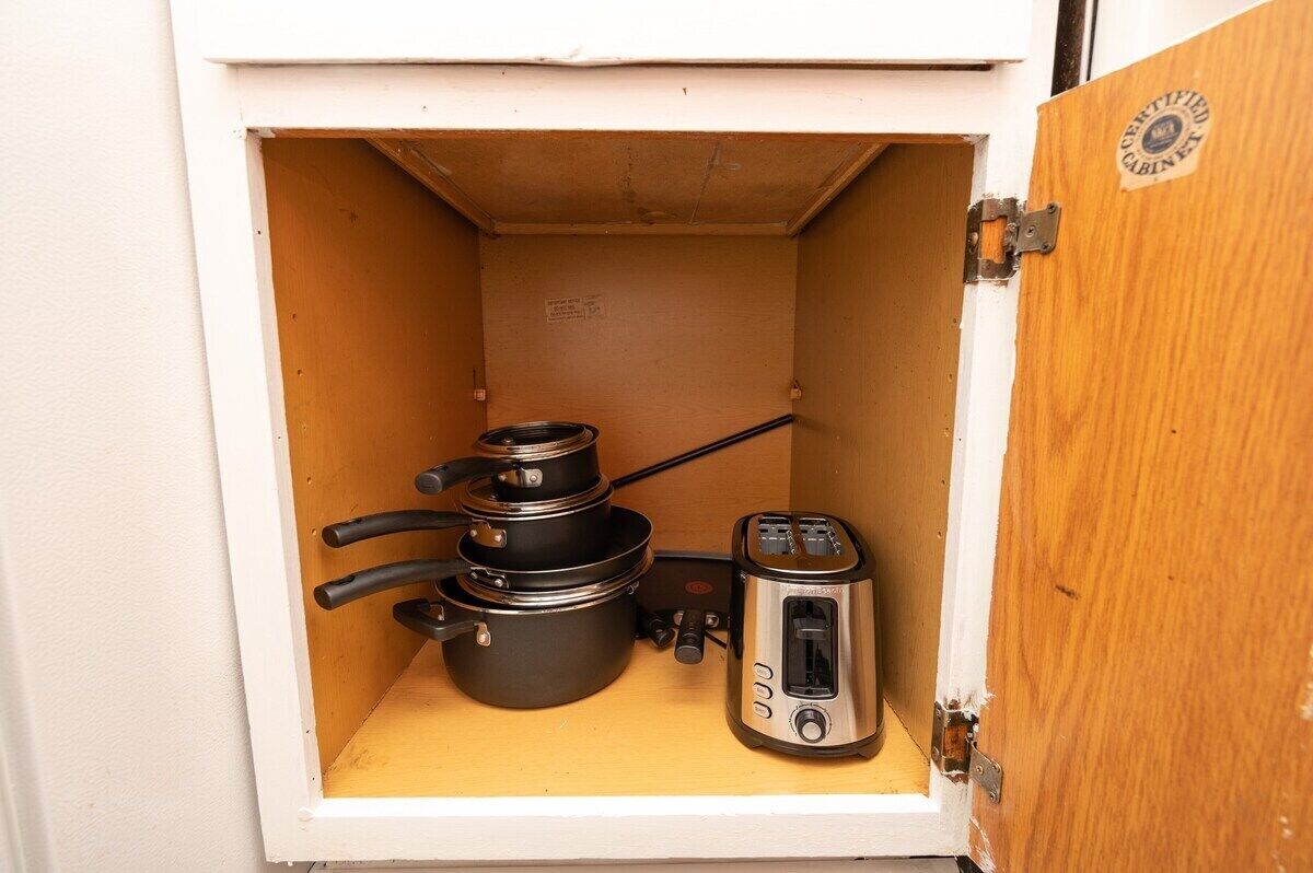Una kitchenette compacta con tostadora, hervidor y set de ollas sobre una estante.