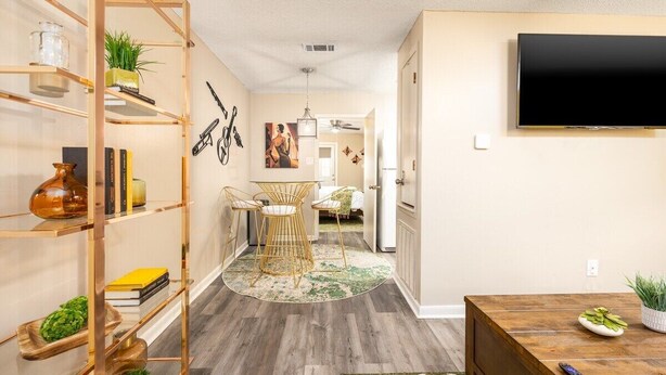 A modern living room with a wooden coffee table, a TV mounted on the wall, and a bookshelf with decorative items.