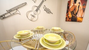 A dining area with a glass table and gold chairs, surrounded by wall art including musical instruments and a painting.