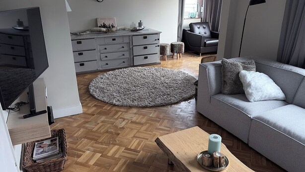 A modern living room with a grey sofa, a wooden coffee table, a grey rug, a grey dresser, and a black chair.