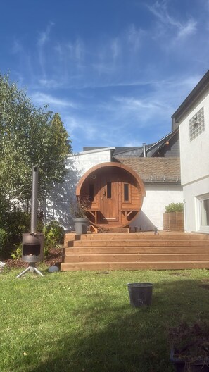 A wooden barrel structure with steps leading up to it, a metal grill, and a clear blue sky. - Villa Annabelle, a luxury vacation home in Winterberg (Winterberg)