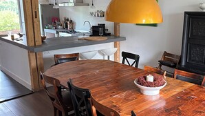 A modern kitchen with a wooden island, a dining table with chairs, and a yellow pendant light.