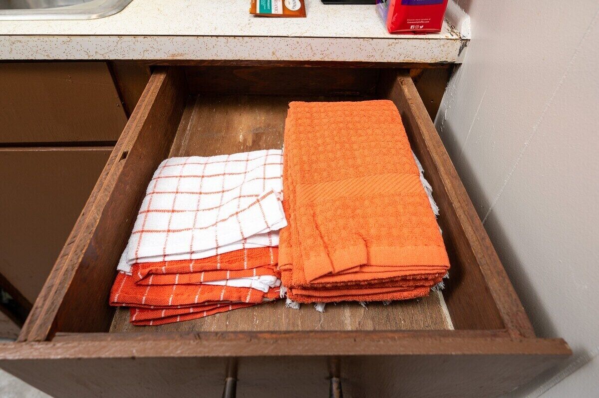 A kitchen drawer with two folded towels, one orange and one white with red stripes.