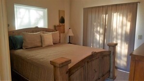 A bedroom with a wooden bed, a nightstand, a lamp, and a window with curtains. - Mountain Hideaway (Ruidoso)