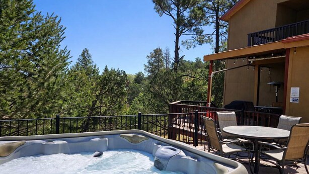 A hot tub on a wooden deck with outdoor furniture, surrounded by trees. - Mountain Hideaway (Ruidoso)