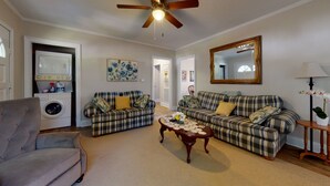 A living room with two plaid sofas, a wooden coffee table, a grey armchair, a ceiling fan, a large mirror, and a washing machine. - Convenient to everything!! (Cartersville)