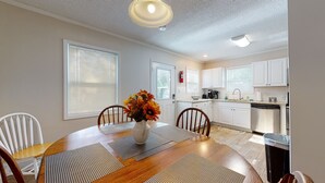 A dining area with a wooden table, chairs, and a vase with flowers. There is a kitchen area with white cabinets and a sink. - Convenient to everything!! (Cartersville)