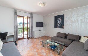 Relax in this stylish living room with a sofa, flat-screen TV, and glass coffee table, leading to a balcony with a terrace.