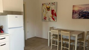 Ett kök med ett vitt kylskåp, ett matbord med fyra stolar och två tavlor på väggen.