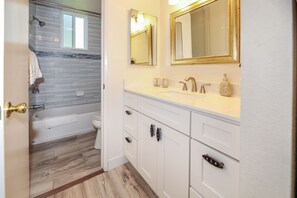 A bathroom with a bathtub, a toilet, and a vanity with a sink and mirrors.