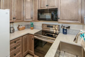 A kitchen with wooden cabinets, a stainless steel microwave, a built-in oven, and a blender on the counter.