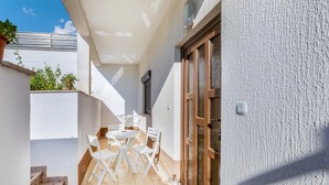 Eine kleine Terrasse im Freien mit einem weißen Tisch und Stühlen, einer Holztür und einem kleinen Fenster.