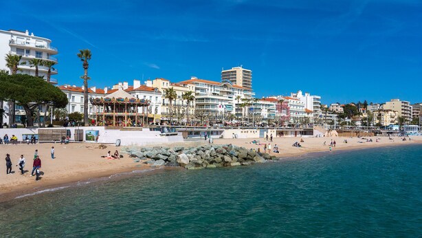 A coastal cityscape with a sandy beach, clear blue waters, and a variety of buildings including hotels and residential structures.