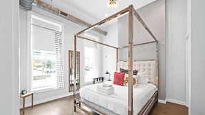 A four-poster bed in a modern room with large windows, a wooden floor, and a view of the outside. - 4 Apartments, Downtown, Walk to Cincy Stadiums! (Covington)