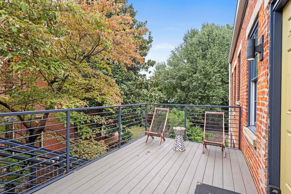 A wooden deck with a metal railing, surrounded by trees with autumn foliage.