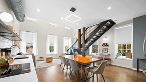 A modern kitchen with a wooden dining table, grey chairs, and a staircase with a metal railing. - 4 Apartments, Downtown, Walk to Cincy Stadiums! (Covington)