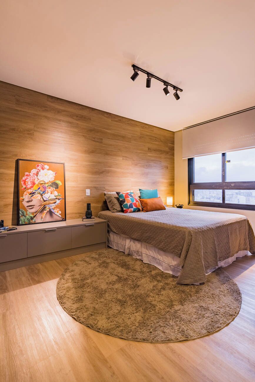 A modern bedroom with a large bed, a wooden headboard, a painting, a bedside table, and a window.