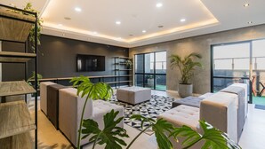 A modern living room with a black and white patterned floor, grey sofas, a TV mounted on the wall, and large windows offering a view of the outdoors. - Century Park by My Way (Porto Alegre)