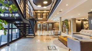 A modern hotel lobby with a staircase, seating area, and a reception desk. - Century Park by My Way (Porto Alegre)