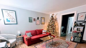 A living room with a red sofa, a coffee table, a Christmas tree, and a framed picture of a raccoon on the wall. - Yinzer House - Hike and Ski (Jay)