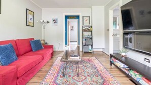 A living room with a red sofa, a coffee table, a TV, and a bookshelf. - Yinzer House - Hike and Ski (Jay)