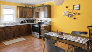 A kitchen with wooden cabinets, a stove, and a dining table with chairs. - Yinzer House - Hike and Ski (Jay)