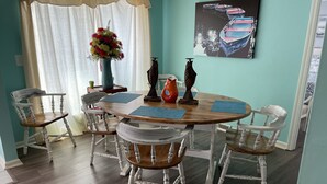 A dining area with a round wooden table, white chairs, a vase of flowers, and a painting on the wall. - Mid lake, pet friendly 4 bedroom, 3 bath with protected swim area (Dadeville)