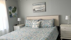 A bedroom with a patterned bedspread, a ceiling fan, a nightstand with a lamp, a wall-mounted painting, and a window with curtains. - Mid lake, pet friendly 4 bedroom, 3 bath with protected swim area (Dadeville)