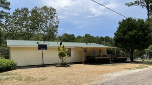 A single-story building with a green roof, a satellite dish, and a basketball hoop in front. - Mid lake, pet friendly 4 bedroom, 3 bath with protected swim area (Dadeville)