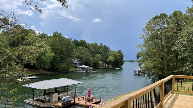 A deck overlooking a calm lake with docked boats, surrounded by lush greenery and a house in the background. - Mid lake, pet friendly 4 bedroom, 3 bath with protected swim area (Dadeville)