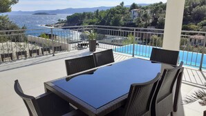 A terrace with a glass table and wicker chairs, overlooking a pool and a coastal view. - Holiday Hvar LUX 2.  (Vrbanj)