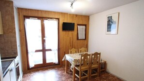 A dining area with a wooden table and chairs, a television on the wall, and a door leading to an outdoor space. - Ground floor, tv, ski locker, 23m², Val Cenis (Lanslevillard)
