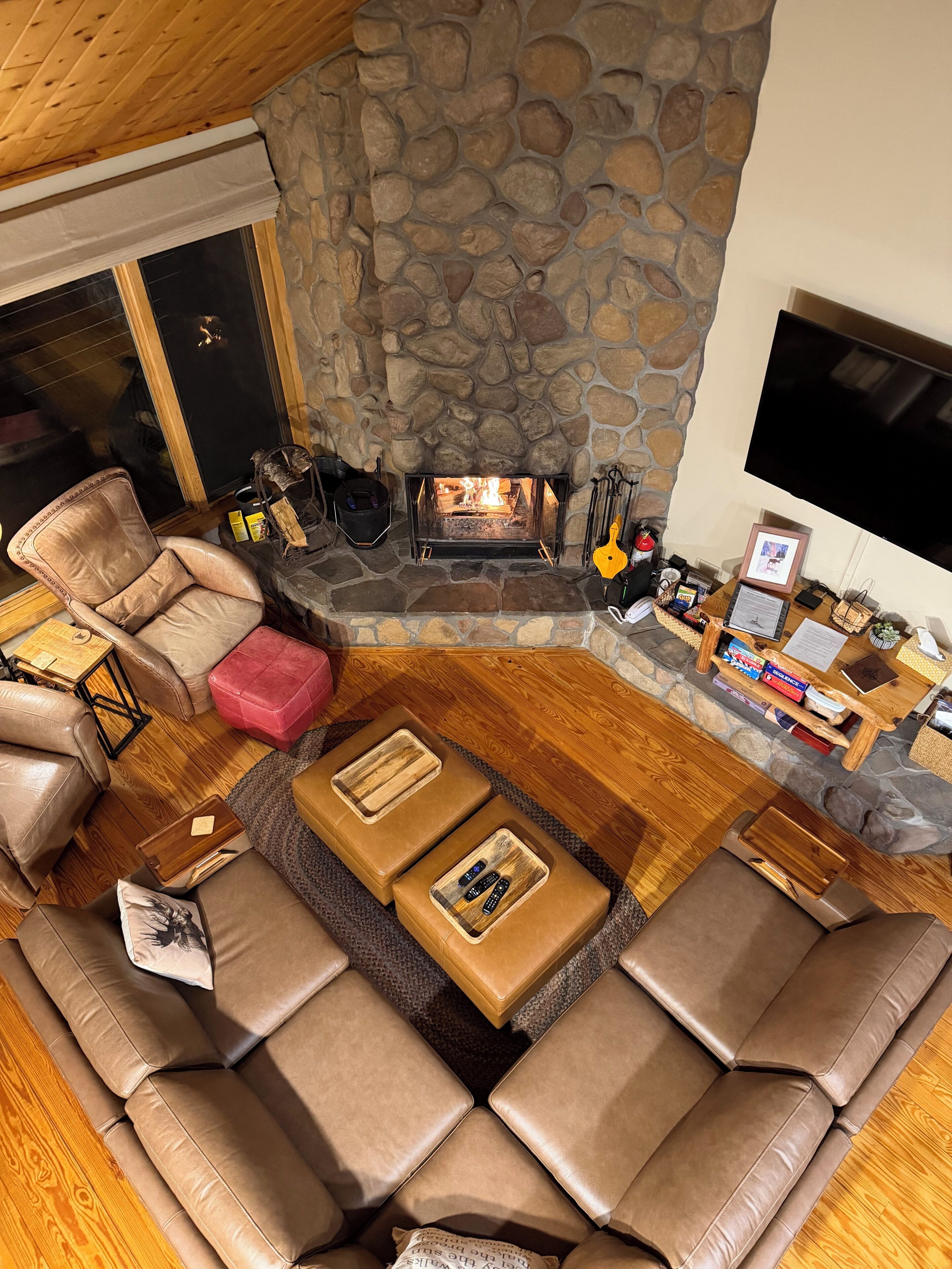 A cozy living room with a stone fireplace, leather sofas, a flat-screen TV, and a stone wall.