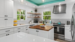 Una cocina moderna con armarios blancos, una isla de madera y un techo color turquesa.