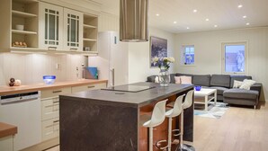 A modern kitchen with a central island, bar stools, a dining area with a sofa, and a large window. - Nice home in Sandve with house sea view (Sandve)