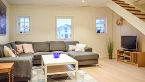 A living room with a sectional sofa, a coffee table, a TV on a wooden stand, and a staircase. - Nice home in Sandve with house sea view (Sandve)