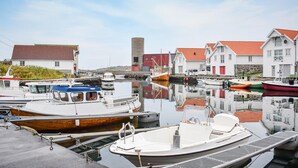A marina with boats docked, a white building with a red roof, and a stone structure in the background. - Nice home in Sandve with house sea view (Sandve)