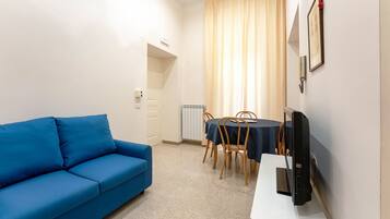 Ein Zimmer mit einem blauen Sofa, einem Esstisch mit Stühlen und einem Flachbildfernseher auf einem Lowboard.
