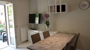 Ein Essbereich mit Tisch, Stühlen, Fernseher, einer Uhr und einer Blumenvase.