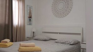 Habitación de hotel con cama, dos almohadas, mesita de noche, lámpara, cuadro y un adorno en la pared.