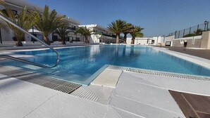 Una piscina con una escalera de metal, palmeras y un cielo azul despejado.