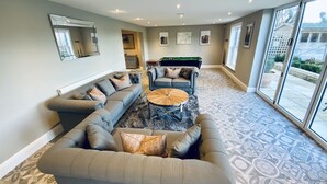 A spacious living area with a large L-shaped sectional sofa, a round coffee table, and a pool table.