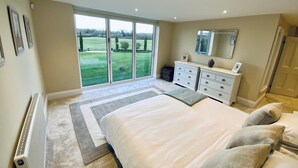 A bedroom with a large bed, a dresser, a mirror, and a view of a green landscape through the window.