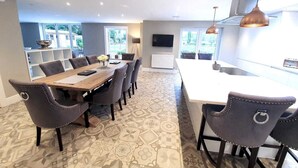 A modern kitchen with a large island, dining area with a long table and chairs, and a view of the outdoors through large windows.