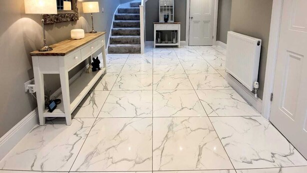 A spacious hallway with marble flooring, a wooden console table with lamps, a mirror, and a staircase leading to another level.